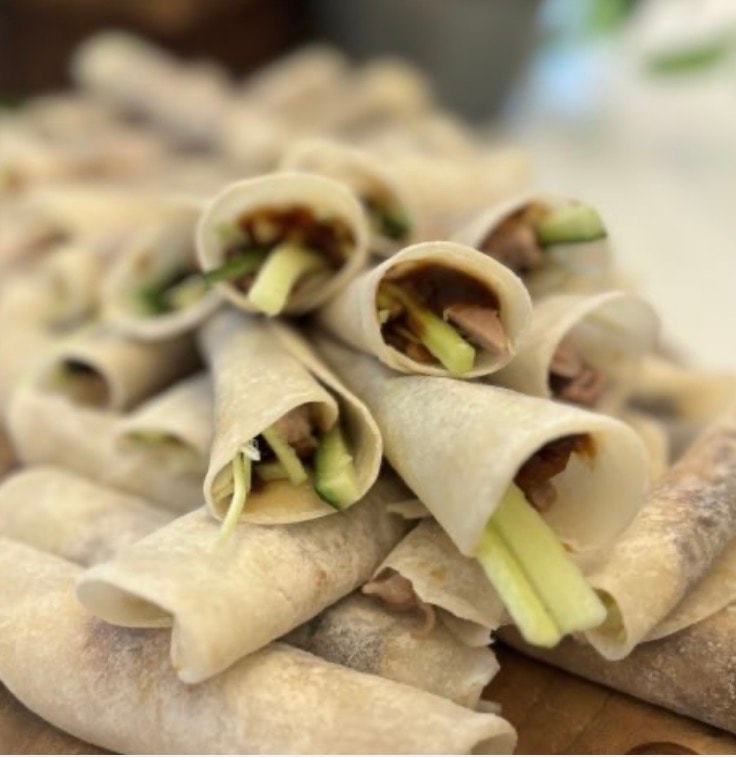 Peking duck pancake rolls piled on a board at a catering event