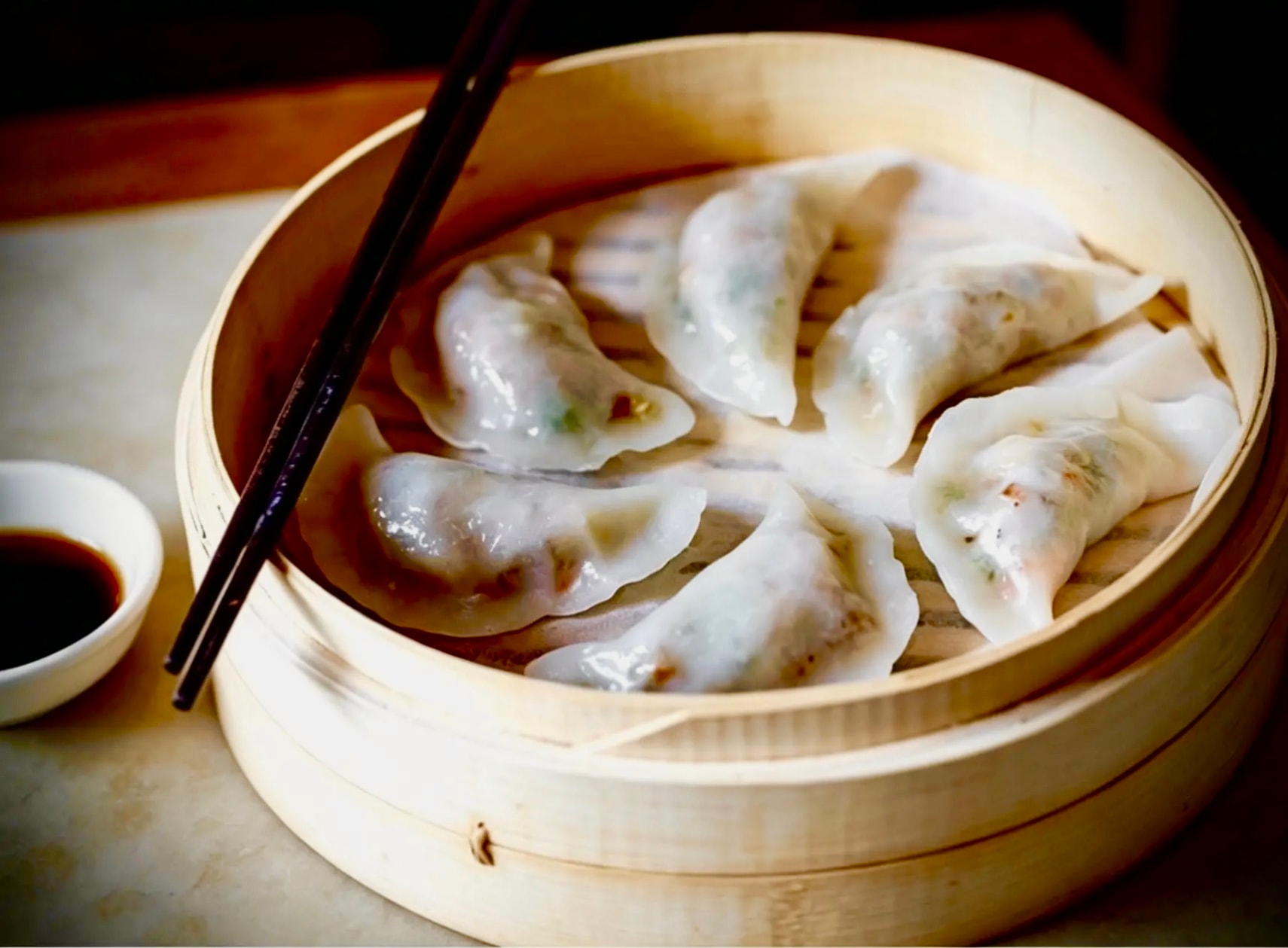 Handmade dumplings in a bamboo steamer with chopsticks and soy dipping sauce