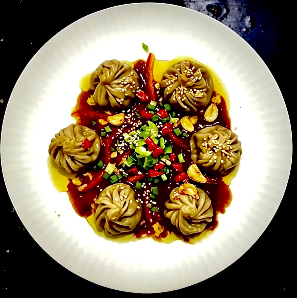 Dumplings in chilli oil with sesame, scallion and garlic on a white plate